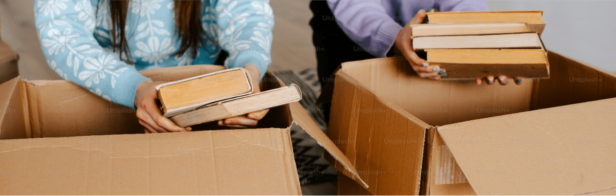 Two women packing books into cardboard boxes