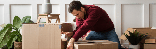 Man securing family belongings in a cardboard box with tape